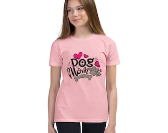 Può includere: T-shirt rosa chiaro con la scritta "Dog Mom" in corsivo, accompagnata da un design con impronta di zampa e osso. Il design include cuori rosa e impronte di zampe. La maglietta è a maniche corte.