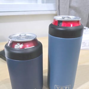 Könnte beinhalten: Zwei marineblaue YETI-Kühlbehälter, einer mit einer Dr. Pepper-Dose. Die Kühler haben einen schwarzen Gummiaufsatz und das YETI-Logo unten. Die Dosen sind rot und silber.