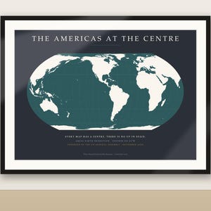 May include: A framed wall map titled THE AMERICAS AT THE CENTRE, featuring a white world map on a dark teal background. The text below reads EVERY MAP HAS A CENTRE. THERE IS NO UP IN SPACE. EQUAL EARTH PROJECTION - CENTRED ON 90°W.