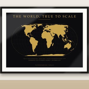 May include: A framed wall art print featuring a black background with a gold-colored world map in an equal earth projection. The text at the top reads THE WORLD, TRUE TO SCALE, with additional small text at the bottom detailing the projection.