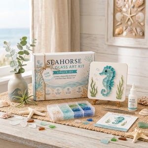 Peut inclure: Un kit d'art en verre de mer représentant un hippocampe dans une boîte blanche avec des graphismes bleus et verts, comprenant une toile carrée avec une mosaïque d'hippocampe, des morceaux de verre, de la colle, une pince et un guide.