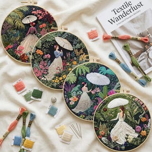 Op de afbeelding: Vier ronde houten borduurringen met gedetailleerd naaiwerk van figuren met parasols in weelderige, kleurrijke tuinen. De set bevat diverse klossen borduurgaren in tinten roze, groen, blauw en geel, samen met een boek.