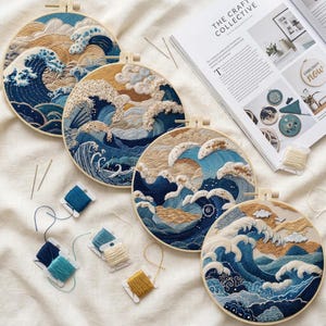 May include: Four circular wooden embroidery hoops featuring intricate needlework of ocean waves in shades of blue, cream, and gold. Several small spools of embroidery thread in blue, cream, and gold colors are scattered alongside the hoops.