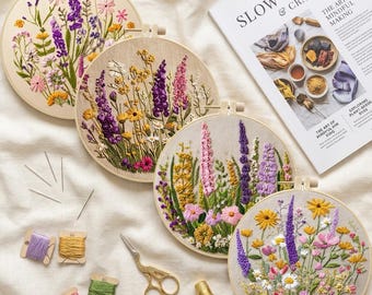 Puede incluir: Cuatro bastidores de bordado circulares de madera con coloridos diseños florales en hilo morado, amarillo y rosa. Incluye un libro titulado Slow Textiles & Craft, tijeras doradas, un dedal y varios carretes pequeños de cartón con hilo.