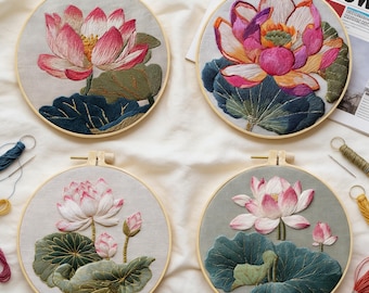 May include: Four round embroidery hoops featuring detailed lotus flower designs. The flowers are pink and white, with green and blue-green leaves. The hoops are set against a neutral background, with visible embroidery threads.
