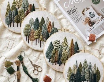 May include: Four circular embroidery hoops featuring hand-stitched forest landscapes with various green and brown trees on white fabric. Included are embroidery floss skeins in shades of green and brown, metal scissors, and sewing needles.