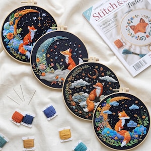 May include: Four circular embroidery hoops featuring fox designs on black fabric, each depicting a fox sitting on a crescent moon or clouds with stars. Includes embroidery needles and several spools of colored thread, plus a Stitch & Story magazine.