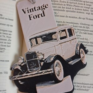 May include: A vintage-style bookmark featuring a classic Ford car design. The bookmark is light pink with a black car silhouette and the words "Vintage Ford" in black. The bookmark is made of a sturdy material and has a string for easy placement.