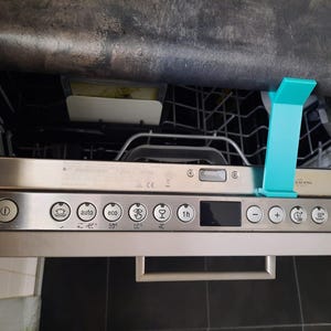 Peut inclure: Un lave-vaisselle en acier inoxydable avec un support en plastique turquoise. Le panneau de commande comporte divers boutons et un affichage numérique. Le lave-vaisselle est ouvert, révélant les paniers intérieurs.