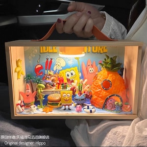 Op de afbeelding: Een rechthoekige houten displaydoos met een oranje handvat met een miniatuurscène met SpongeBob SquarePants-personages, een ananashuis, een burger en een klein lampje aan de bovenkant, met de tekst IDLE ADVENTURE zichtbaar.