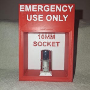 May include: A red 3D-printed box with the words "EMERGENCY USE ONLY" in white. Inside, a white background displays "10MM SOCKET" and a silver 10mm socket. The box is designed to hold the socket.