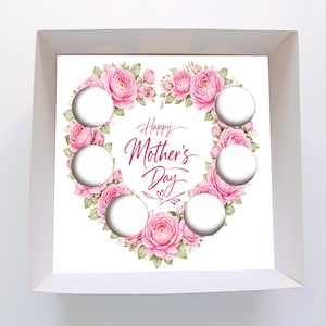 Puede incluir: Una caja blanca con un diseño de corazón floral para el Día de la Madre. El corazón está compuesto por rosas rosas y hojas verdes, rodeando el texto "Happy Mother's Day". Hay seis recortes circulares.