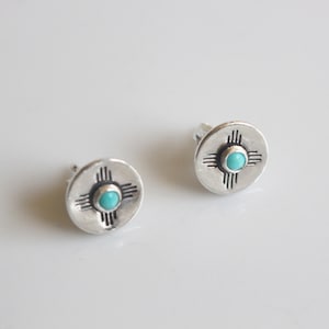 May include: A pair of silver earrings with a turquoise stone in the center of each earring. The earrings feature a southwestern design.