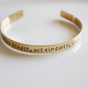 May include: Gold-toned metal bracelet with the inscription "Speak kindly. Act sincerely. Choose love."
