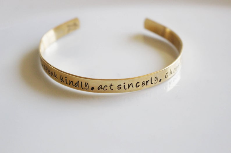 May include: Gold-toned metal bracelet with the inscription "Speak kindly. Act sincerely. Choose love."