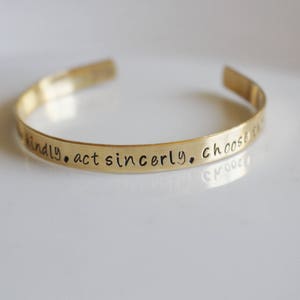 May include: Gold-toned metal bracelet with the inscription "be kindly. act sincerely. choose to be..."
