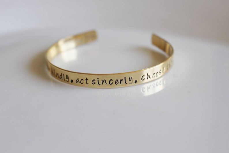 May include: Gold-toned metal bracelet with the inscription "be kindly. act sincerely. choose to be..."