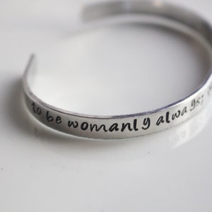 May include: Silver bracelet with the inscription "to be womanly always is not to be weak".