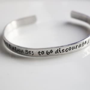 May include: Silver bracelet with the inscription "to be discouraged is always; to be courageous is to be always"