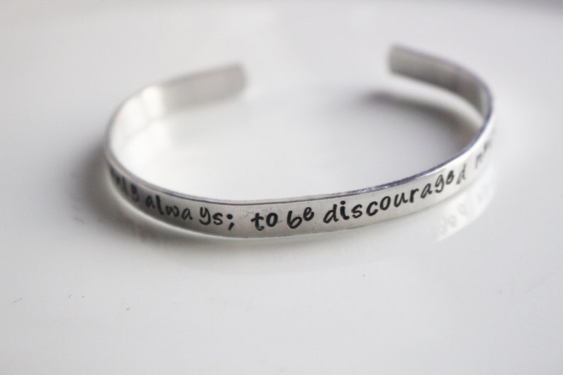 May include: Silver bracelet with the inscription "to be discouraged is always; to be courageous is to be always"