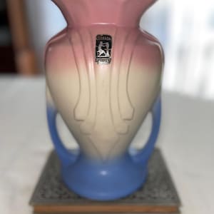 Puede incluir: Un jarrón de cerámica vintage con una combinación de colores degradados, que va del rosa en la parte superior al blanco en el medio y al azul en la base. El jarrón tiene dos asas y una etiqueta decorativa "Granada Pottery".