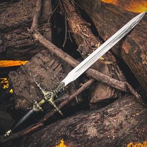 May include: A silver sword with an ornate gold and black hilt rests on a pile of weathered logs. The blade is long and sharp, reflecting light. The hilt features intricate details, suggesting a fantasy or historical theme.