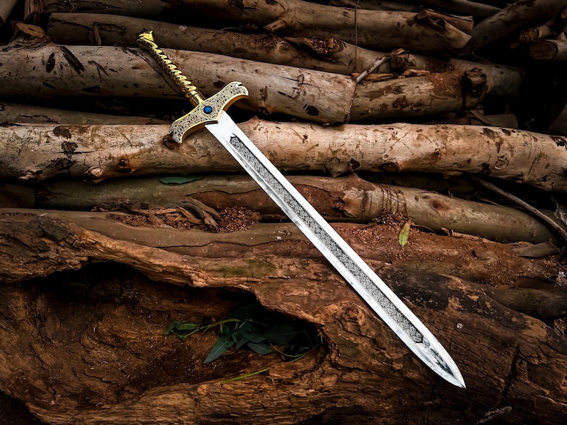 May include: An ornate sword with a gold-colored hilt and a silver blade, resting on a bed of wooden logs. The hilt features intricate designs and a blue gem. The blade has a detailed pattern. The sword is a fantasy or historical item.