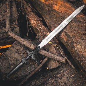 May include: A silver sword with a black handle and ornate crossguard rests on a pile of weathered logs. The blade is long and sharp, reflecting the light. The sword's handle features intricate details.