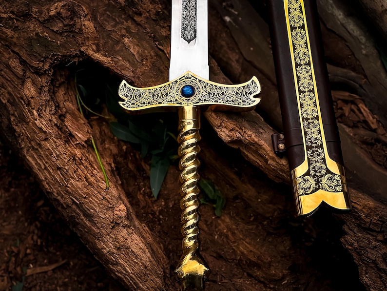May include: A decorative sword with a gold-colored handle and crossguard, featuring intricate patterns and a blue gem. The blade is silver, and the scabbard is brown with gold accents. The sword is displayed against a textured, brown background.