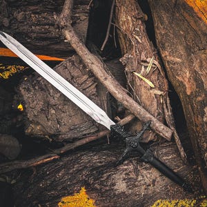 May include: A long, silver sword with a black handle and ornate guard rests on a bed of weathered wood. The blade is sharp and reflective, contrasting with the dark, textured background. The sword's design suggests a fantasy or historical theme.