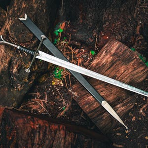 May include: A silver sword with a black handle and a black sheath rests on a weathered wooden surface. The sword features intricate details on the hilt and a sharp blade. The scene evokes a fantasy or historical theme.
