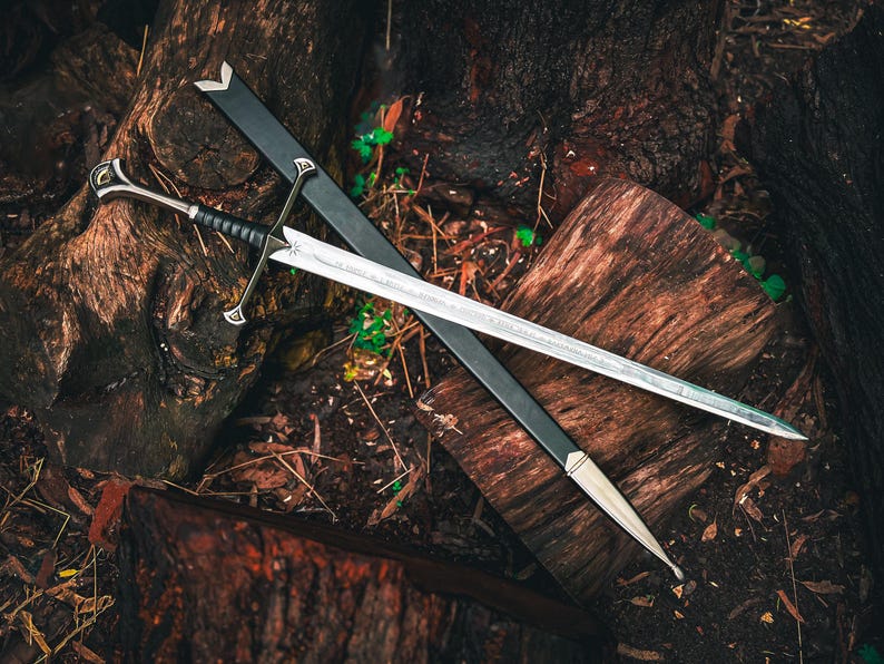 May include: A silver sword with a black handle and a black sheath rests on a weathered wooden surface. The sword features intricate details on the hilt and a sharp blade. The scene evokes a fantasy or historical theme.