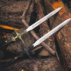 May include: Two decorative swords with ornate handles and silver blades rest on a bed of wood. One sword features a gold-colored handle with intricate detailing, while the other has a black handle. The blades are long and pointed.
