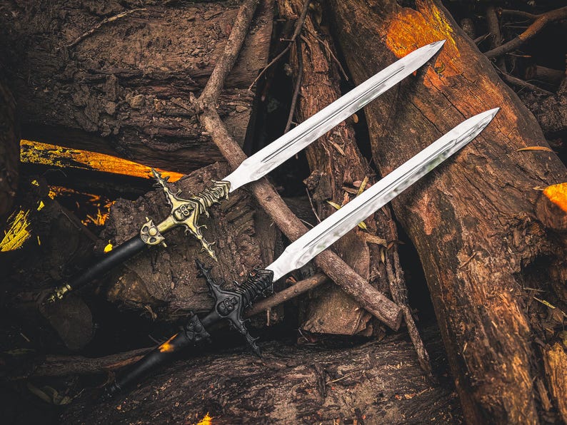 May include: Two decorative swords with ornate handles and silver blades rest on a bed of wood. One sword features a gold-colored handle with intricate detailing, while the other has a black handle. The blades are long and pointed.