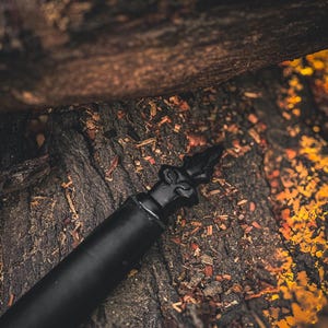 May include: A black bottle stopper with a decorative top, set against a textured, dark brown background. The stopper's design features an ornate, pointed finial. The image has a warm, earthy tone.