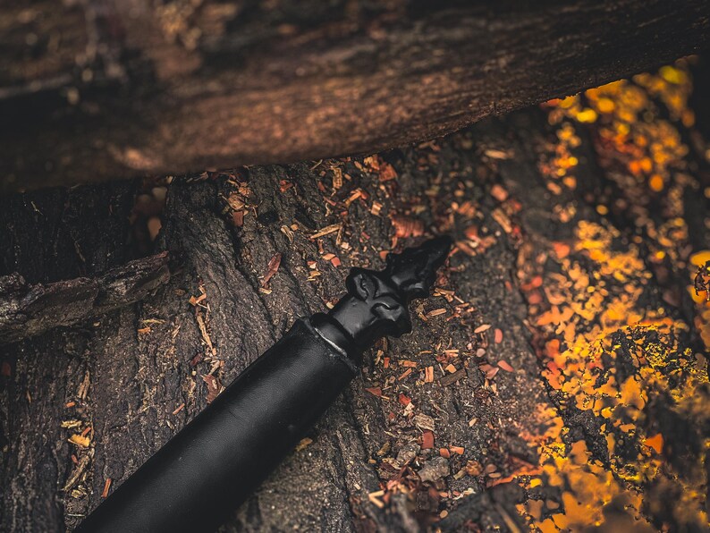 May include: A black bottle stopper with a decorative top, set against a textured, dark brown background. The stopper's design features an ornate, pointed finial. The image has a warm, earthy tone.