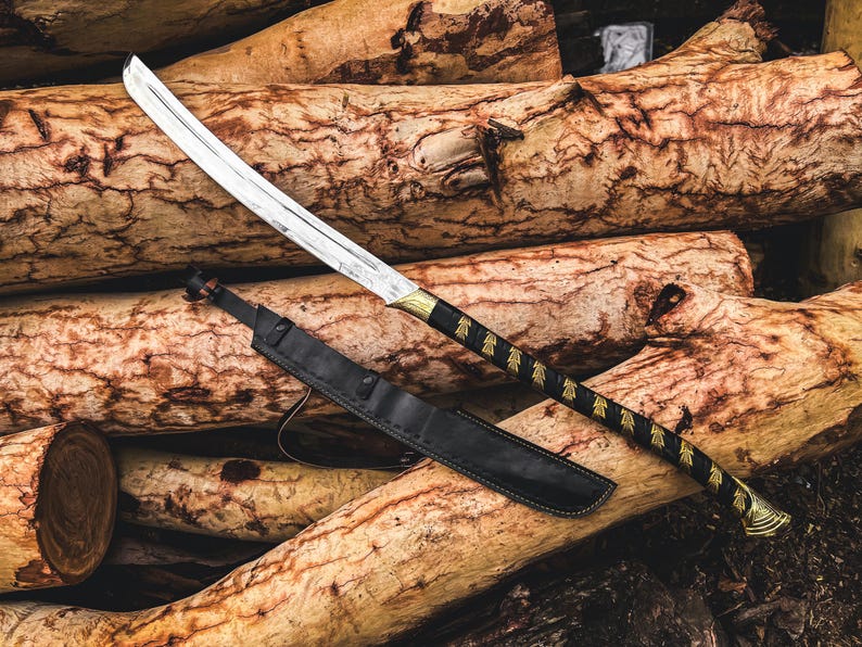 K&ouml;nnte beinhalten: Ein Katana-Schwert mit silberner Klinge und schwarzem Griff mit goldenen Akzenten liegt auf einem Stapel Holzscheite. Eine schwarze Lederscheide liegt neben dem Schwert. Der Griff des Schwertes hat ein dekoratives Muster.