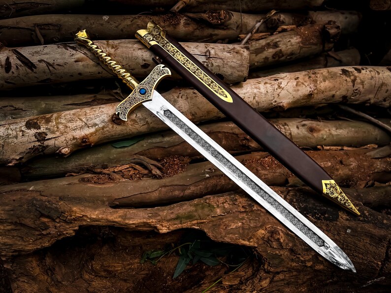 May include: A decorative sword with a silver blade and ornate gold hilt, featuring a blue gem. The sword rests on a bed of wooden logs, with a brown sheath adorned with gold accents. The sword's design suggests a medieval or fantasy theme.