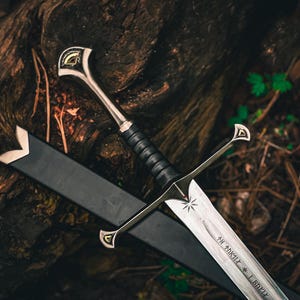 May include: A detailed image of a silver sword with a black handle and a black sheath. The sword has a star design on the blade and intricate detailing on the hilt. The sword is resting on a dark, textured surface, possibly wood.