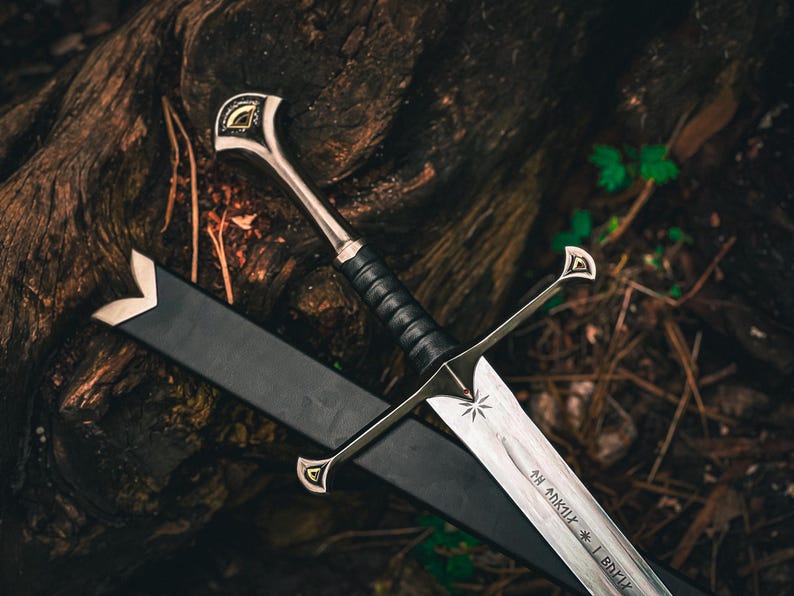 May include: A detailed image of a silver sword with a black handle and a black sheath. The sword has a star design on the blade and intricate detailing on the hilt. The sword is resting on a dark, textured surface, possibly wood.