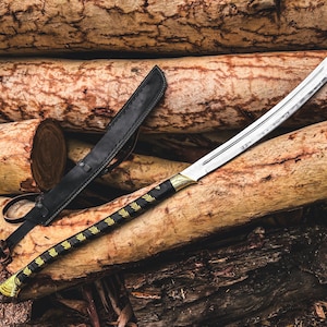 K&ouml;nnte beinhalten: Ein gebogenes Schwert mit einer silbernen Klinge und einem schwarz-goldenen Griff liegt auf einem Holzstapel. Eine schwarze Lederscheide befindet sich links vom Schwert. Der Griff des Schwertes hat ein dekoratives Golddesign.