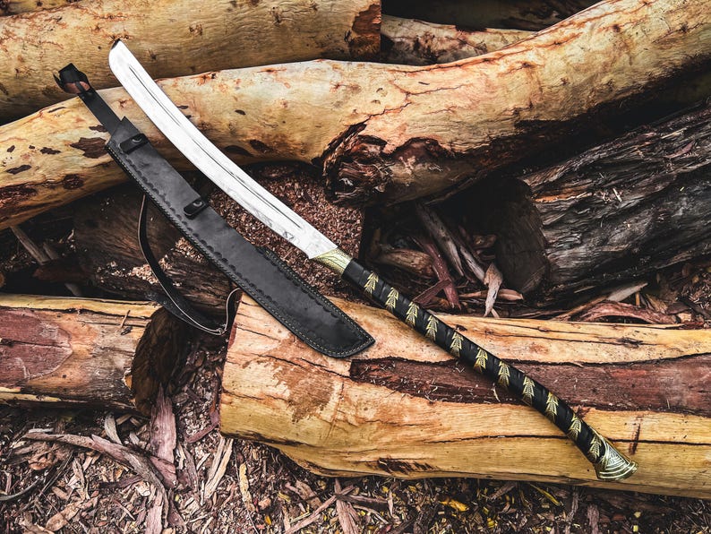 K&ouml;nnte beinhalten: Ein gebogenes Schwert mit einer silbernen Klinge und einem schwarz-goldenen Griff, das auf einem Stapel Holzst&auml;mme liegt. Das Schwert befindet sich in einer schwarzen Lederscheide. Der Griff ist mit schwarzem Leder mit goldenen Akzenten umwickelt.