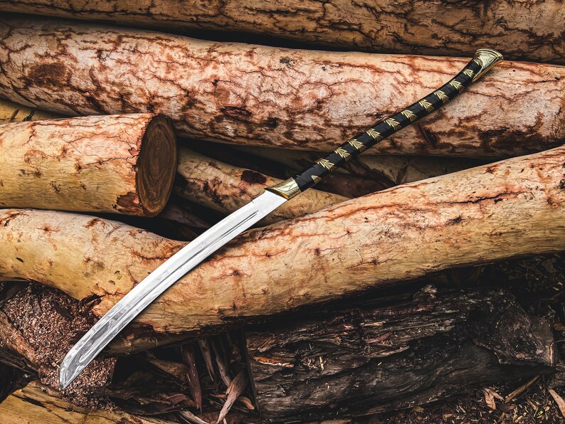 K&ouml;nnte beinhalten: Ein Katana-Schwert mit einer silbernen Klinge und einem schwarz-goldenen Griff. Das Schwert liegt auf einem Stapel Holzscheite. Der Griff hat eine schwarze Wicklung mit goldenen Akzenten.