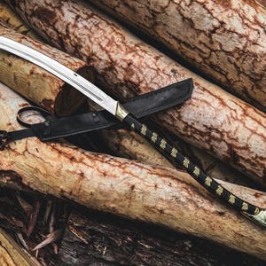 K&ouml;nnte beinhalten: Ein Katana-Schwert mit gebogener Klinge, schwarzem Griff und goldenen Akzenten, das auf einem Stapel Holzst&auml;mme liegt. Das Schwert befindet sich in einer schwarzen Lederscheide. Der Griff hat ein dekoratives Muster.