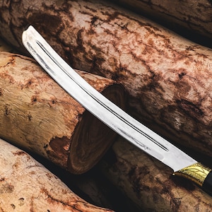 K&ouml;nnte beinhalten: Ein gebogenes Messer mit silberner Klinge und einem schwarzen und goldenen Griff liegt auf einem Stapel Holzst&auml;mme. Die Klinge hat eine scharfe Schneide und ein dekoratives Design am Griff. Die St&auml;mme sind braun und haben eine raue Textur.