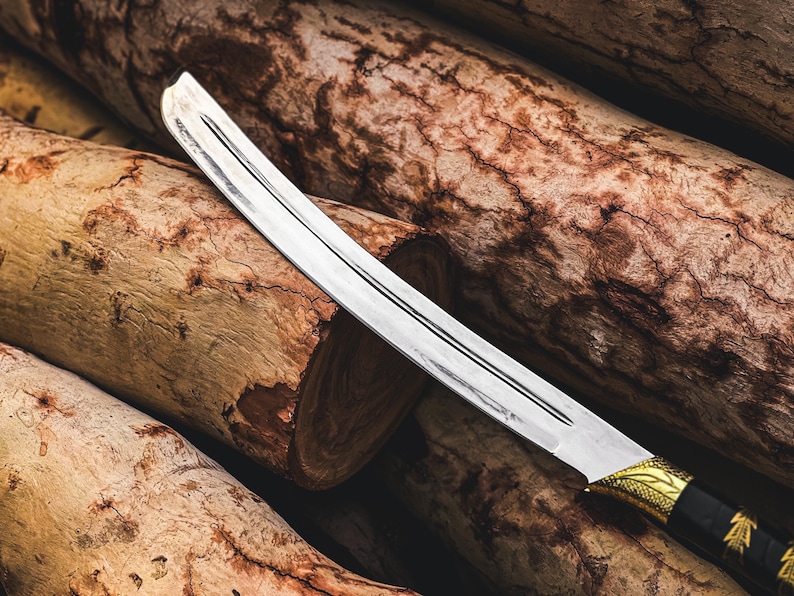 K&ouml;nnte beinhalten: Ein gebogenes Messer mit silberner Klinge und einem schwarzen und goldenen Griff liegt auf einem Stapel Holzst&auml;mme. Die Klinge hat eine scharfe Schneide und ein dekoratives Design am Griff. Die St&auml;mme sind braun und haben eine raue Textur.