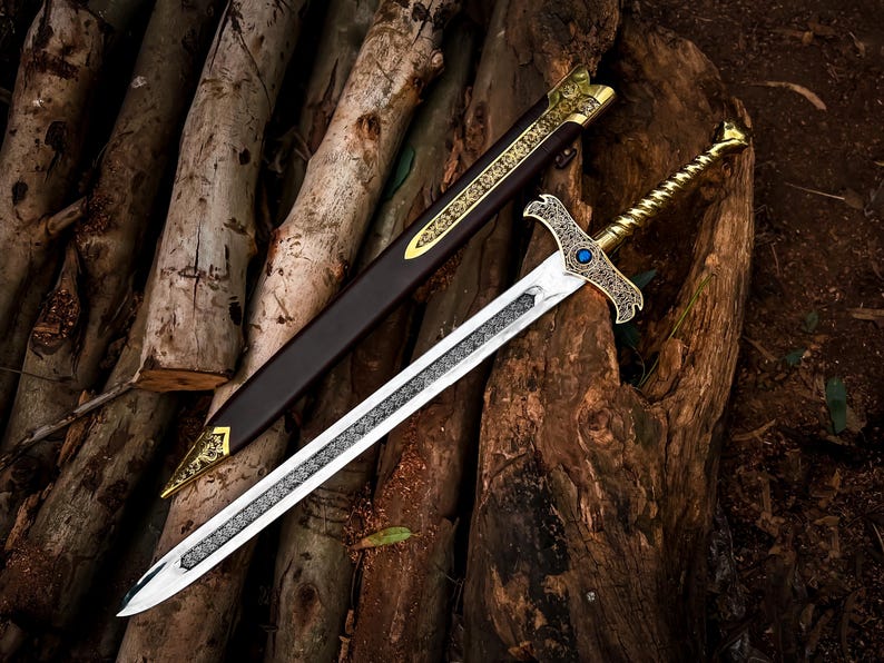 May include: A decorative sword with a silver blade and ornate gold hilt, resting on a wooden surface. The sword has a detailed design and a blue gem. A brown sheath with gold accents lies beside it.