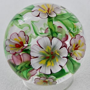 May include: A clear glass paperweight with a floral design. The flowers are white, pink, and yellow with green leaves.