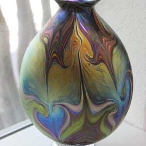 May include: A round iridescent glass vase with a swirling pattern of blue, green, gold, and purple. The vase has a clear glass base.