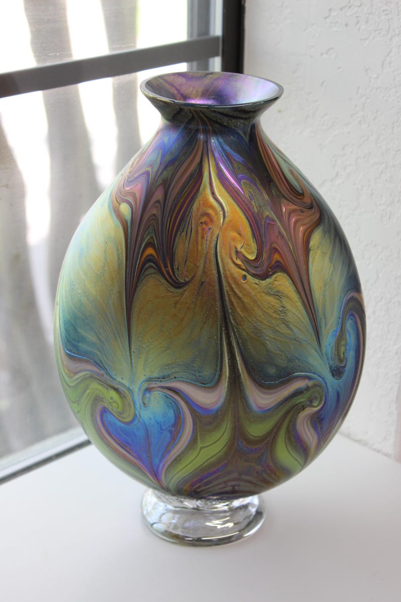 May include: A round iridescent glass vase with a swirling pattern of blue, green, gold, and purple. The vase has a clear glass base.